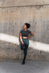 Fototapeta premium Active woman taking a rest after outdoor workout, resting against a concrete wall
