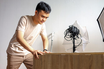 Asian Man Setting up Photography Studio Lights on Wooden Table