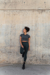 Fototapeta premium Young sporty woman wearing sportswear leaning against a concrete wall looking away
