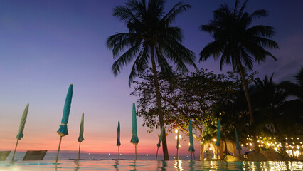 Tourists relaxing in an infinity pool at a luxurious tropical resort, enjoying a breathtaking sunset surrounded by palm trees and shimmering fairy lights
