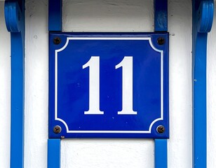 Close-up of a blue house number "11" on a white and blue surface