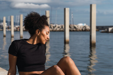 Serene young woman finding peace and tranquility while sitting by the sea, embracing the calming atmosphere of the harbor