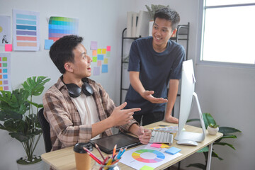 Two Young Asian Graphic Designers Collaborating and Discussing Project at Desk
