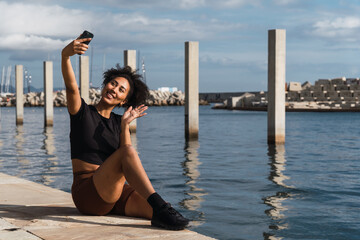 Young woman smiling and waving during a video call on her smartphone by the sunny seaside