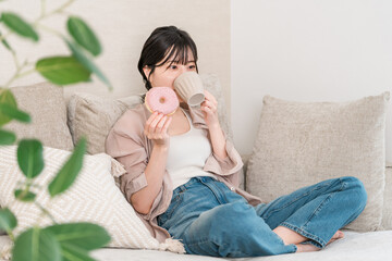 Young Asian woman sitting on a sofa in the living room and eating a donut
