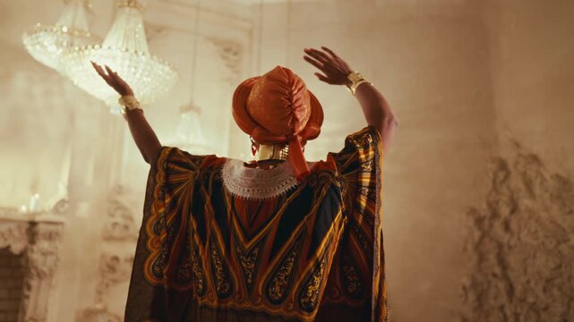 Back view of dancing woman, african shaman or priest praying, asking rain. Amazing dance performance in studio, unique african culture and traditions, bright ethnic gown and turban, unique aesthetics