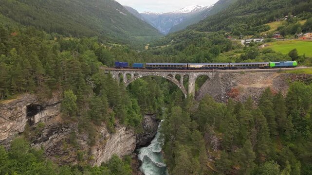 A Train Glides Across a Graceful Stone Arch Spanning a Deep Forested Gorge on the Raumabanen, Crossing Kylling Bru, Norway - Aerial Pullback Shot