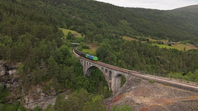 A Train Crosses a Graceful Stone Arch Bridge Above a Forested Gorge, at Kylling Bru on the Raumabanen, Norway - Orbit Drone Shot