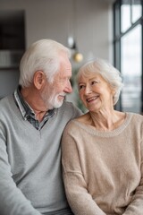 Happy senior couple looking at each other with love and smiling while sitting together in a bright modern apartment, elderly husband and wife enjoying retirement at home