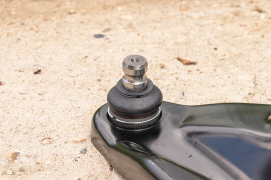 Close-up of a car suspension ball joint on a textured concrete surface.