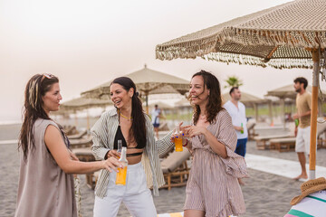 Group of friends laughing and enjoying drinks on a summer beach party at sunset