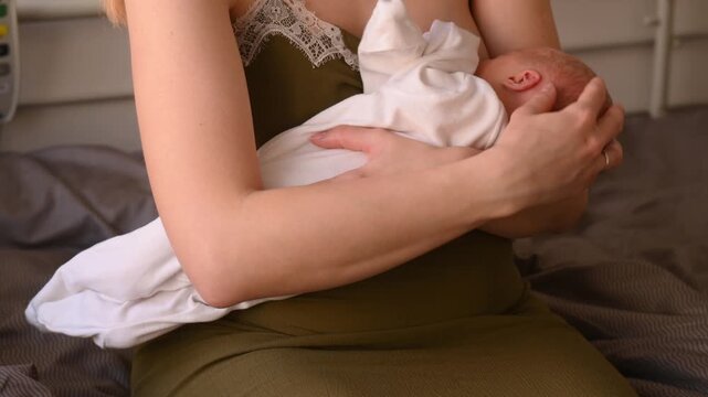 A woman breastfeeds a newborn boy in the maternity hospital. Breastfeeding and rooming-in, early latching, feeding on demand, and avoiding supplemental water.
