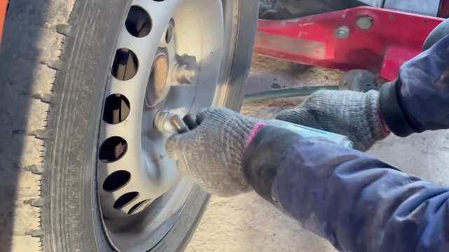 Mechanic unscrewing lug nuts and removing a car wheel with an impact wrench