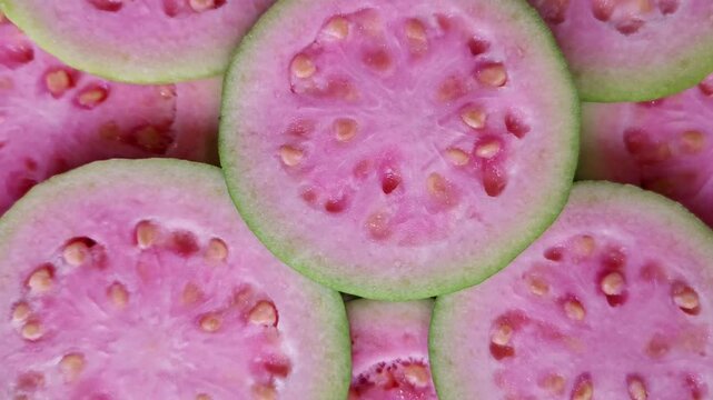 Background close-up footage of fresh red guava slices with smooth rotating movement, showcasing detailed pulp texture, natural seeds, and vibrant red color in a clean fruit visual.