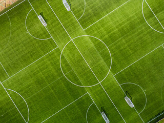 Top-down aerial view of a green football field with white markings and goals. Clean geometric composition, symmetry and texture, outdoor sports and soccer training concept