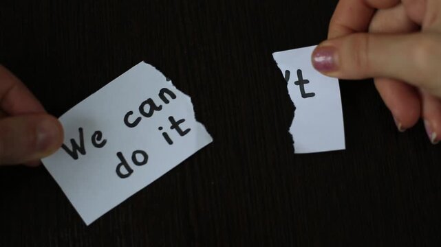 Hands tearing a paper note to change the text from "We can't do it" to "We can do it". Concept of changing impossible to possible, motivation, and removing obstacles
