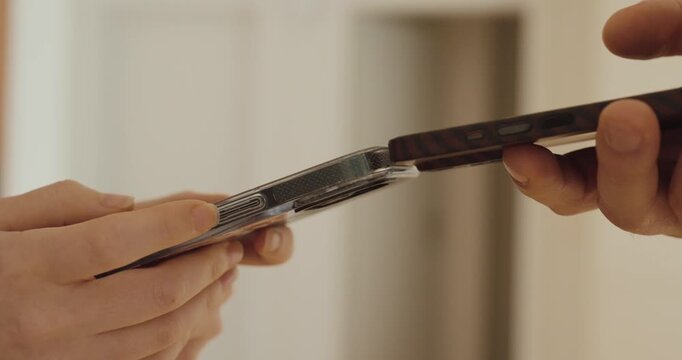 Close-up of two people holding smartphones close together to exchange data &mdash; concept of digital transfer, mobile technology, and wireless communication.