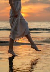 A woman is walking on the beach in a white dress