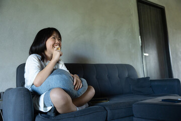 Cute girl relaxing on sofa and eating snack indoors