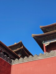 Obraz premium Traditional Chinese palace architecture with red wall and ornate roof details against clear blue sky.