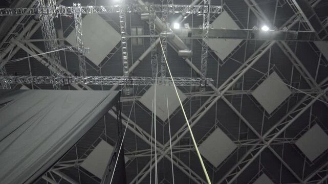 Overhead lights shine on ceiling rigging grid casting intense shadows revealing suspended acoustic panels. Structures shape modern venue