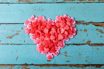 Overhead view of sweet pink and red candies making heart shape on blue wooden table with copy space
