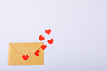 Red heart shapes cutting escaping beige envelope with copy space on white background