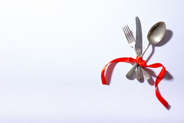 Overhead view of cutlery tied tightly with red ribbon with copy space on white background
