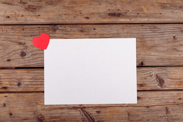 Overhead view of red heart shape at corner of blank white paper with copy space on table