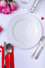 Empty white plate surrounded by pink roses with bottle and cutlery on table