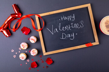 Overhead view of happy valentines day text on writing slate by cupcakes and coffee cup on table