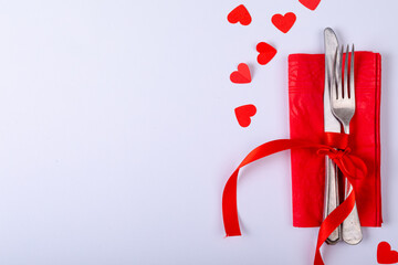 Overhead view of cutlery tied with red ribbon on napkin by copy space over white background