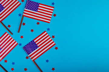 Overhead view of america flag sticks with star shape confetti by copy space on blue background