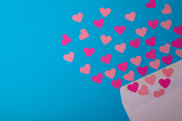 Directly above view of pink hearts coming out from envelope over blue background, copy space