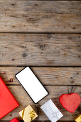 Overhead view of blank screen on smart phone by valentine gifts on table, copy space