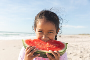 Portrait of cute girl eating large fresh watermelon slice at beach on sunny day © wavebreak3