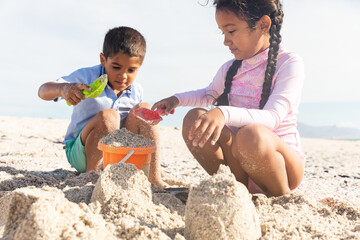 Naklejka premium brother and sister using toys for making sandcastle at beach on sunny day