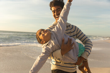 Cheerful man carrying daughter pretending to fly at beach against sky on sunny day