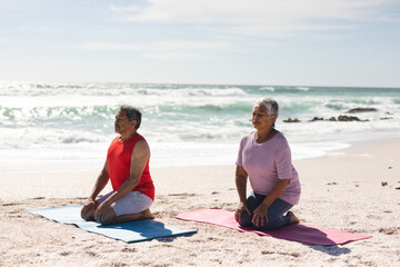 Naklejka premium senior couple meditating while kneeling on yoga mats at beach against sky during sunny day