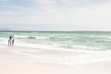 Naklejka premium Full length of multiracial mother and children enjoying sunny weekend on shore at beach