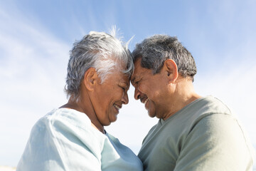 Obraz premium Side view of smiling senior multiracial couple touching forehead at beach during sunny day