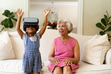 African american grandmother looking at her granddaughter wearing vr headset at home