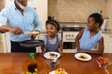 African american grandfather serving breakfast for his two granddaughters in kitchen at home