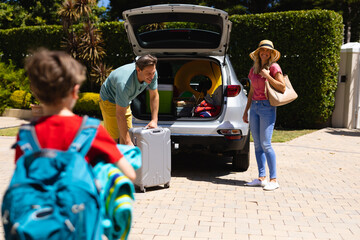 Happy caucasian family putting their luggage in their car outdoors
