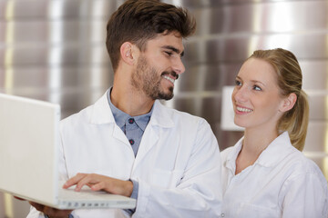 Obraz premium young man and woman wearing labcoats looking at laptop