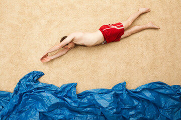 Person in red shorts imitating swimming at beach with blue wave in studio