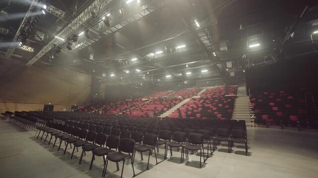 Light fills concert hall highlighting amount of red seats and stage design. Silence creates calm atmosphere before musical performance