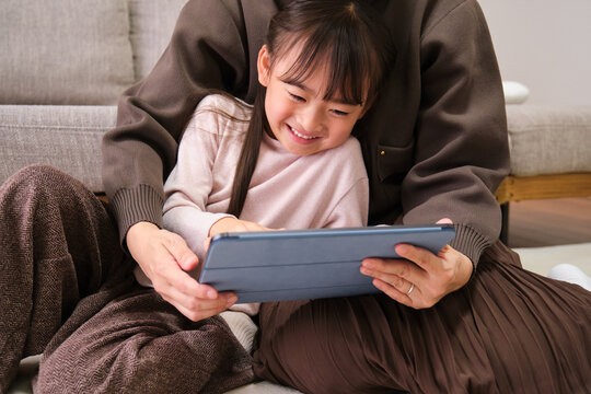 Mother and daughter using tablet together at home in living room
