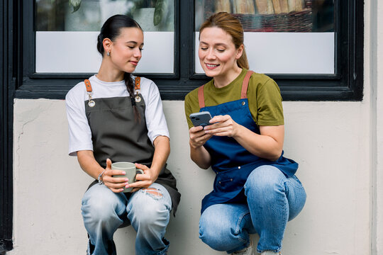 Colleagues on break chatting and using mobile phone in front of bakery