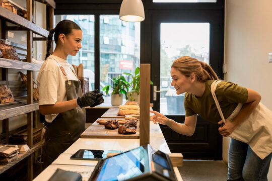 Client choosing bread at bakery counter with shop assistant